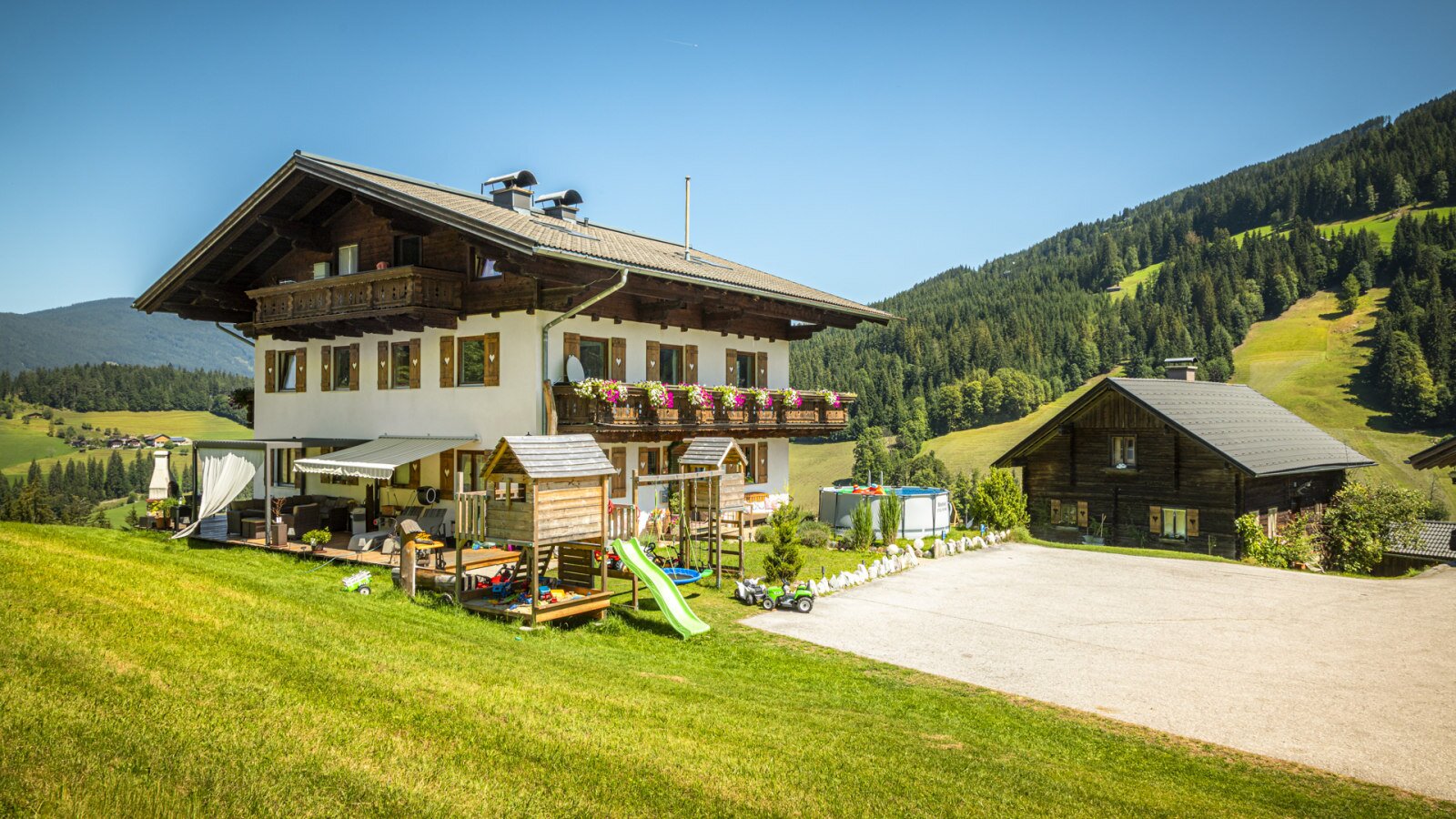 The charming apartment house featuring a spacious, sunny garden with a children's play area, surrounded by scenic green hills.