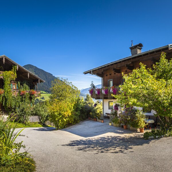 Exterior of the Farm Houses, showcasing traditional wooden architecture with flower-filled balconies, surrounded by lush gardens and mountain scenery.