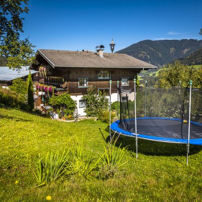 The Farm House exterior features a trampoline in the grassy garden, surrounded by trees and mountains.