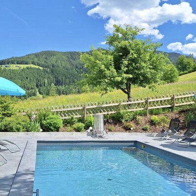 Outdoor pool of the farmhouse with sun loungers, umbrellas, and views of the surrounding mountains.