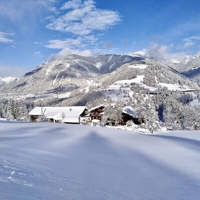 Winter landscape featuring the farmhouse, snow-covered mountains, and forests.