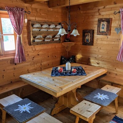 The farmhouse's parlour offers a wooden dining table with built-in benches and additional seating, all within solid wood interiors.