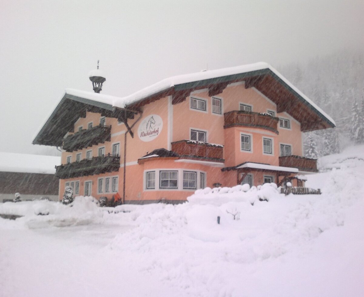 The Farm House exterior covered in snow during winter, featuring balconies and a pitched roof, with snow-covered trees in the background.