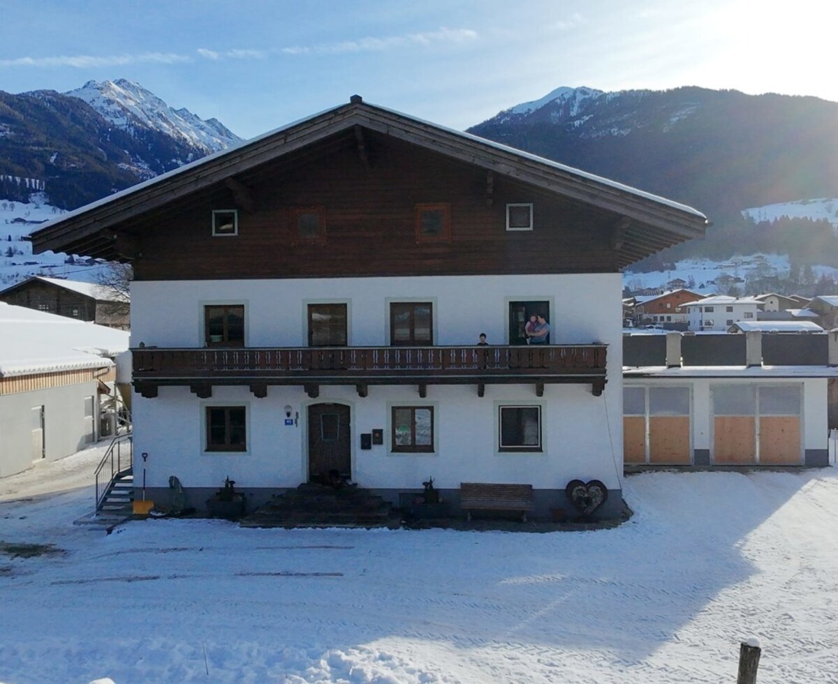 Exterior view of the Zillerlehen farm with a balcony and a snowy mountain landscape in the background.