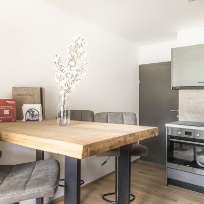 The apartment's kitchen, equipped with an induction hob, oven, and dishwasher, features a dining table with chairs.