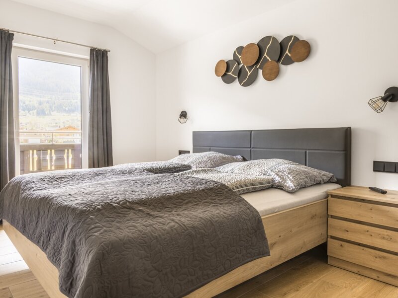Bedroom of the apartment with a double bed, wooden bed frame, bedside table, and balcony access with mountain views.