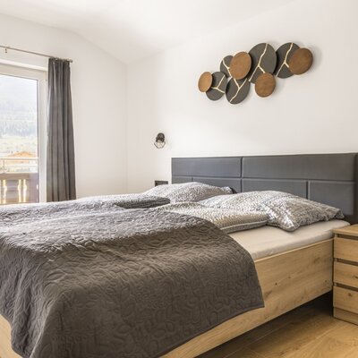 Bedroom of the apartment with a double bed, wooden bed frame, bedside table, and balcony access with mountain views.