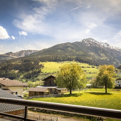 View from the apartment's balcony of the mountain landscape with valley, meadows, and surrounding houses.