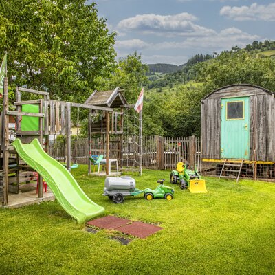 The holiday apartment's inviting playground with a slide, toy tractors, and a green lawn.