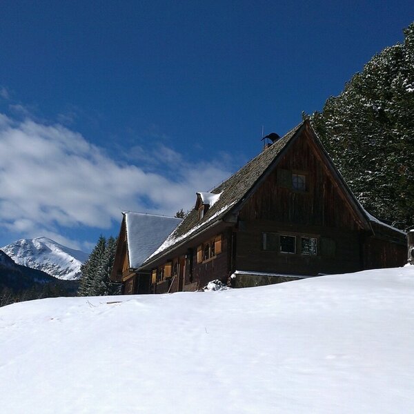 The farmhouse exterior, a wooden building set in a snow-covered mountain landscape.