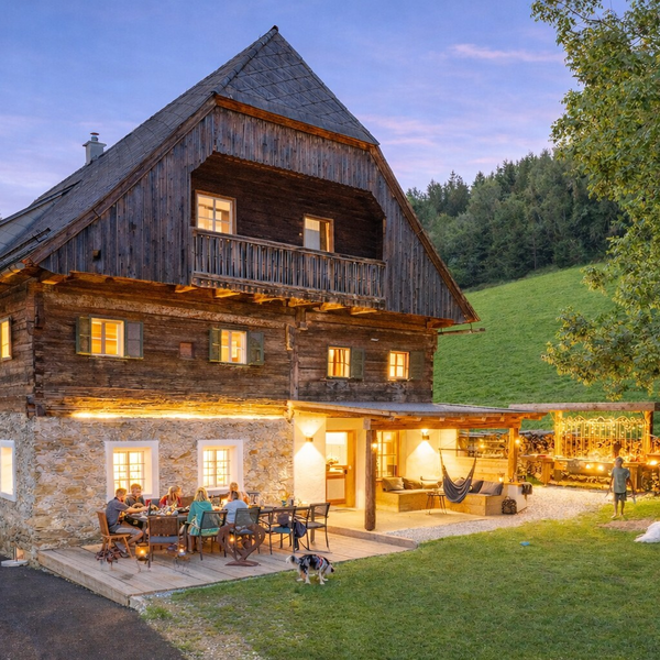 Exterior of the farmhouse featuring an illuminated terrace, outdoor dining area, and a covered lounge in the garden.