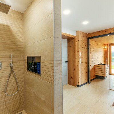 The shower with a rain showerhead and  sauna with wooden benches and lake view.