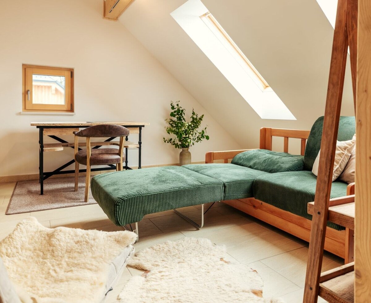 Attic room /open gallery with a green sofa, a desk, and windows.