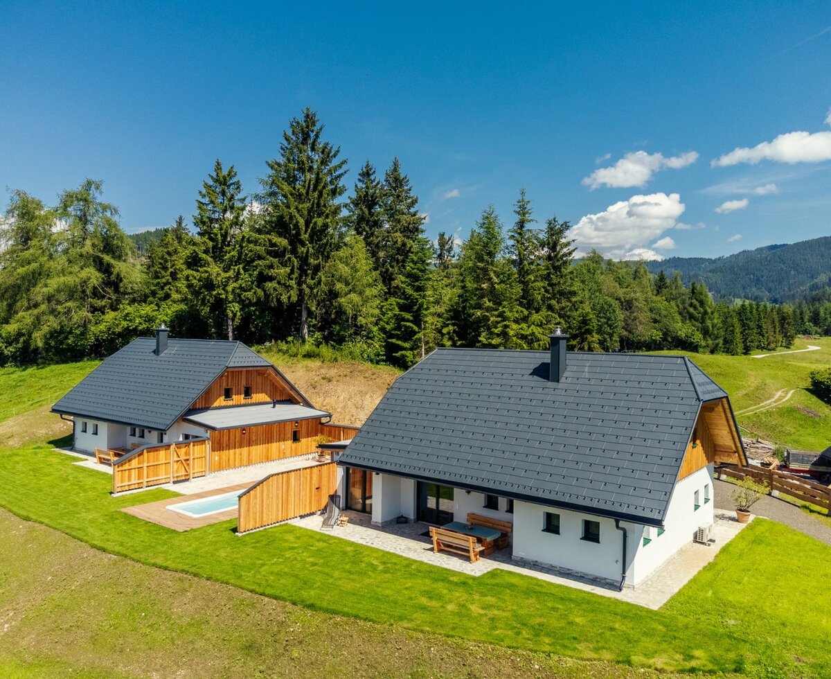 The buildings of the Alpine Chalets Reiter am Berg ...Rubin and Smaragd, surrounded by green meadows and trees, with a small pool area.