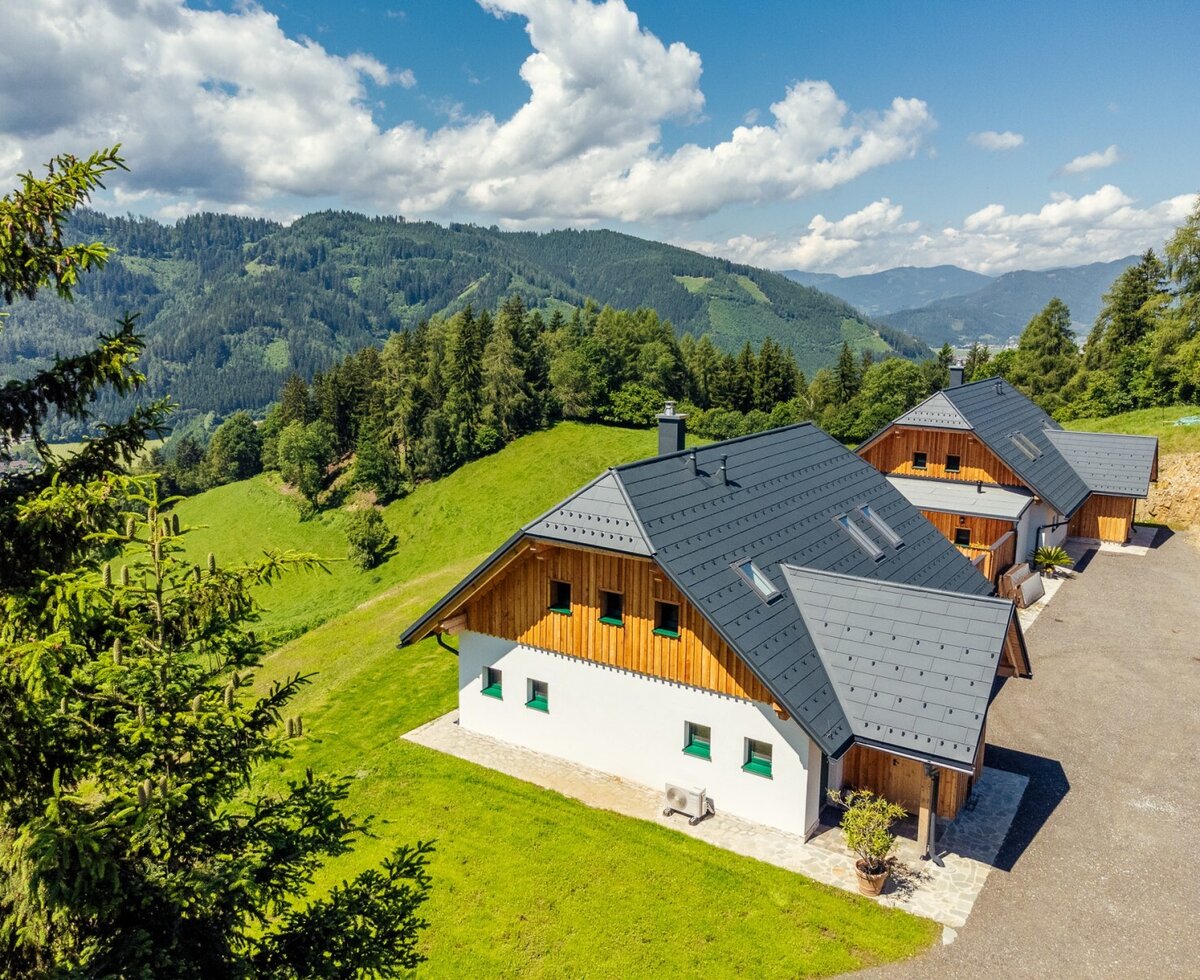parking in front of the Almchalet in a mountain landscape with green hills and forests, accessible via a driveway.