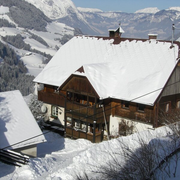 The Farm House exterior with its snow-covered roof and wooden balconies, surrounded by a winter mountain landscape.