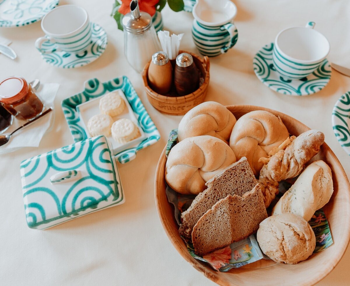 A breakfast table at the Farm House featuring a basket of fresh bread, butter, and jam, alongside patterned ceramic cups.