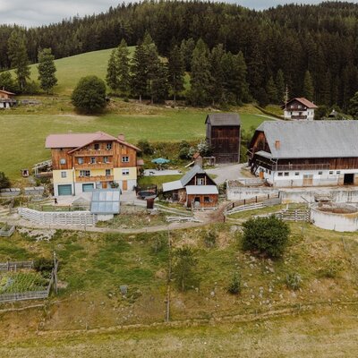 The STUBER Farm House exterior, featuring multiple traditional buildings surrounded by green fields and forested hills.