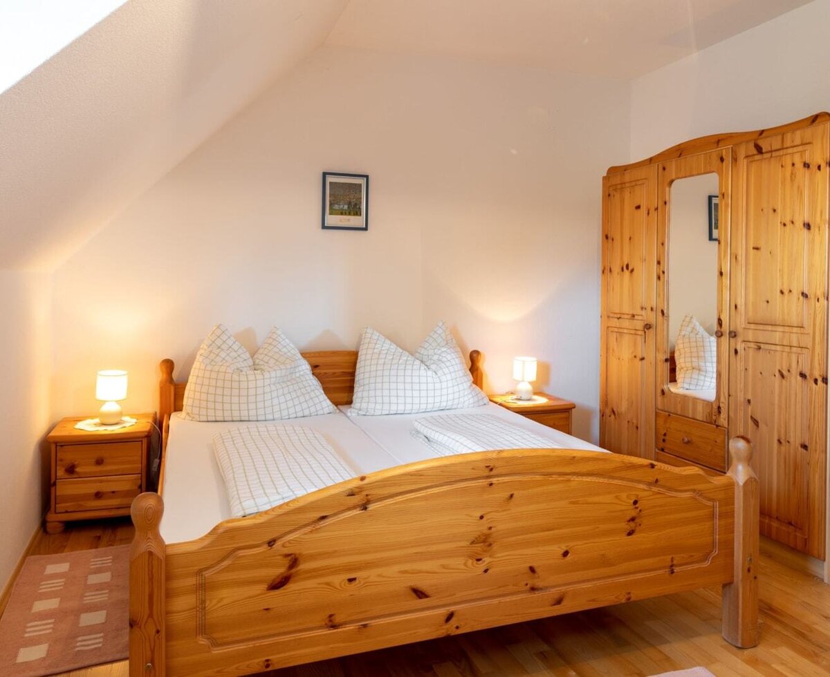 The attic bedroom in the Farm House features a wooden double bed, two nightstands with lamps, and a large wooden wardrobe with a mirror.