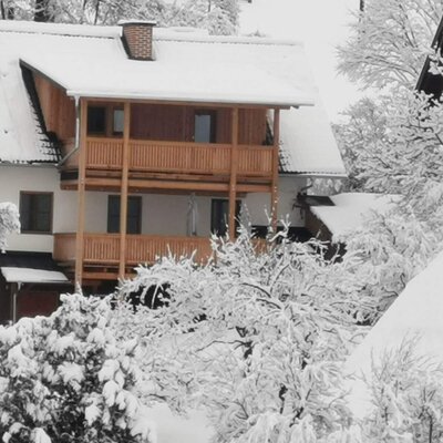The Farm House exterior in winter, featuring wooden balconies and a snow-covered roof and trees.
