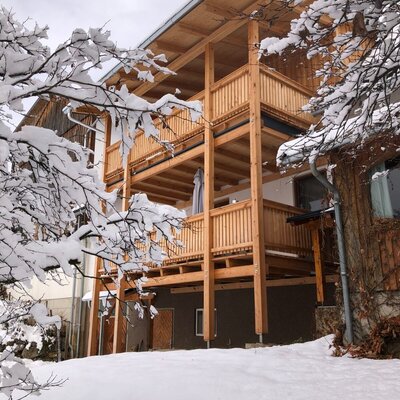 The farmhouse exterior, featuring two levels of wooden balconies, covered in winter snow.