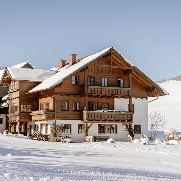 Exterior view of the farmhouse in winter, with a snow-covered roof and balconies.