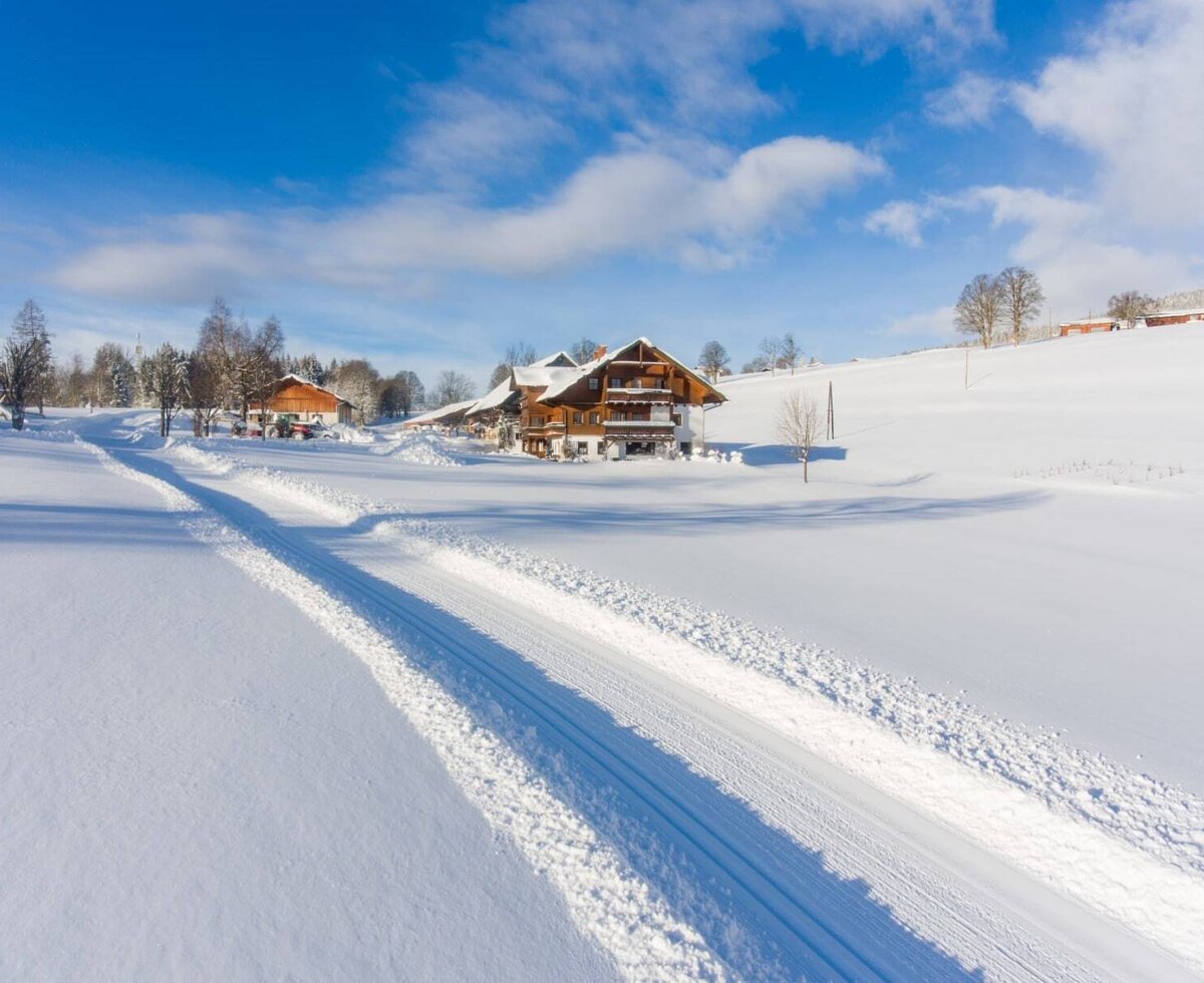 The inviting Bauernhof set in an idyllic, snow-covered winter landscape under a bright blue sky.