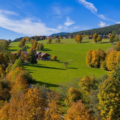 An idyllic farmhouse nestled among lush green meadows and colorful autumn trees.