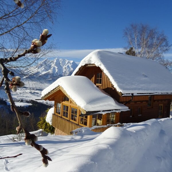 The snow-covered farmhouse with wooden walls and mountain views under a blue sky. The snow-covered farmhouse with wooden walls and mountain views under a blue sky.