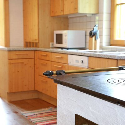 Kitchen in the farmhouse with wooden furnishings, microwave, dishwasher, and a traditional wood-burning stove, adjacent to a dining area.