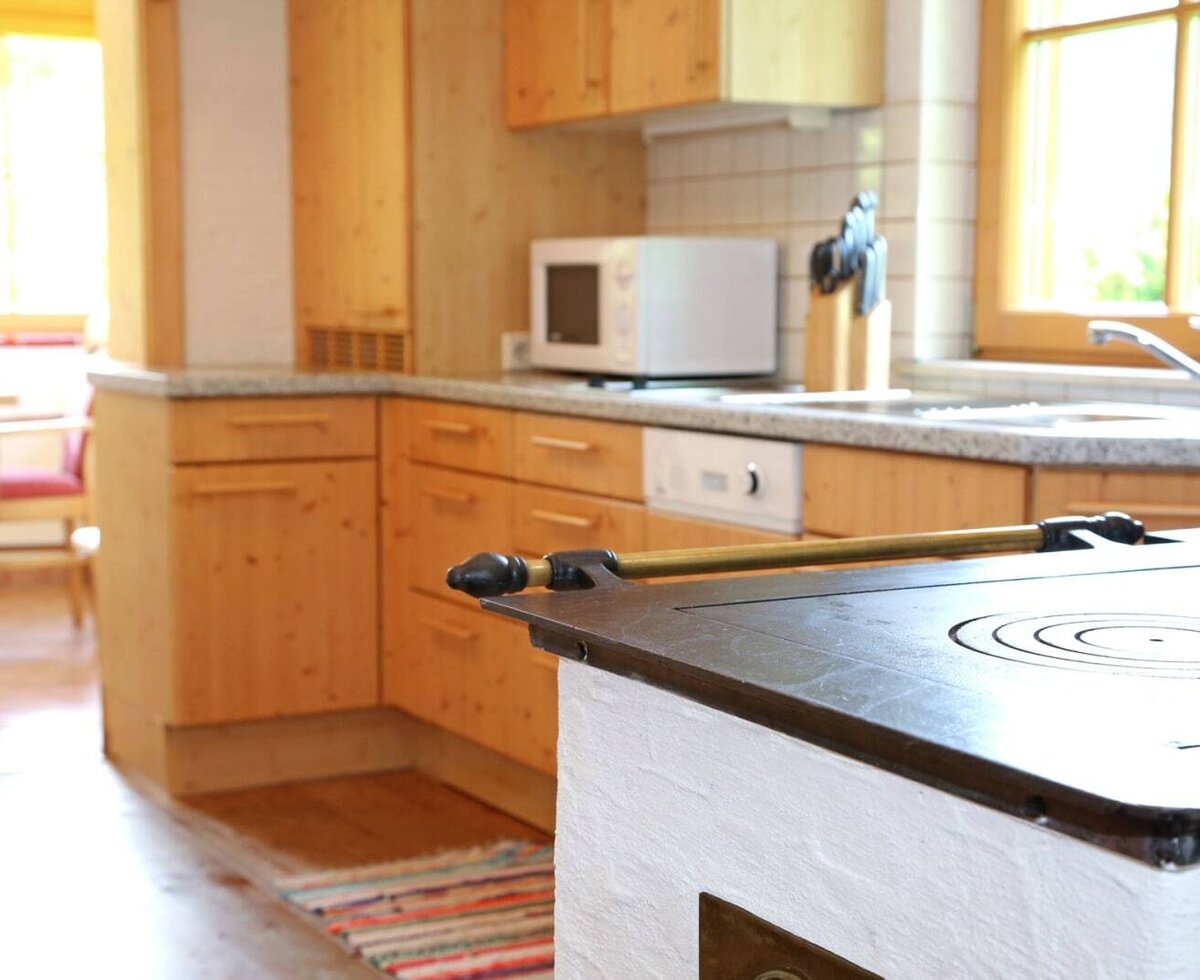 Kitchen in the farmhouse with wooden furnishings, microwave, dishwasher, and a traditional wood-burning stove, adjacent to a dining area.