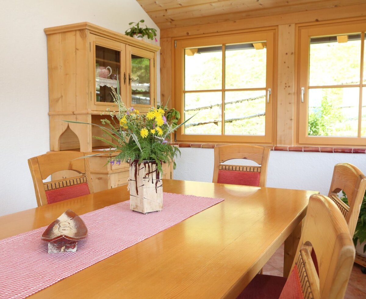 Dining area in the farmhouse, featuring a wooden table, chairs, and windows with a view of nature.