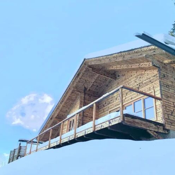 The wooden farmhouse exterior, featuring a balcony with snow and a snow-covered roof.