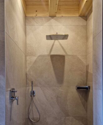 Modern tiled shower in the farmhouse with a rain shower head and a wooden beamed ceiling with lighting.