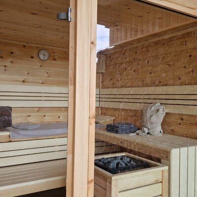 Sauna in the farmhouse with wooden benches, glass door, sauna heater, and a gabion wall.