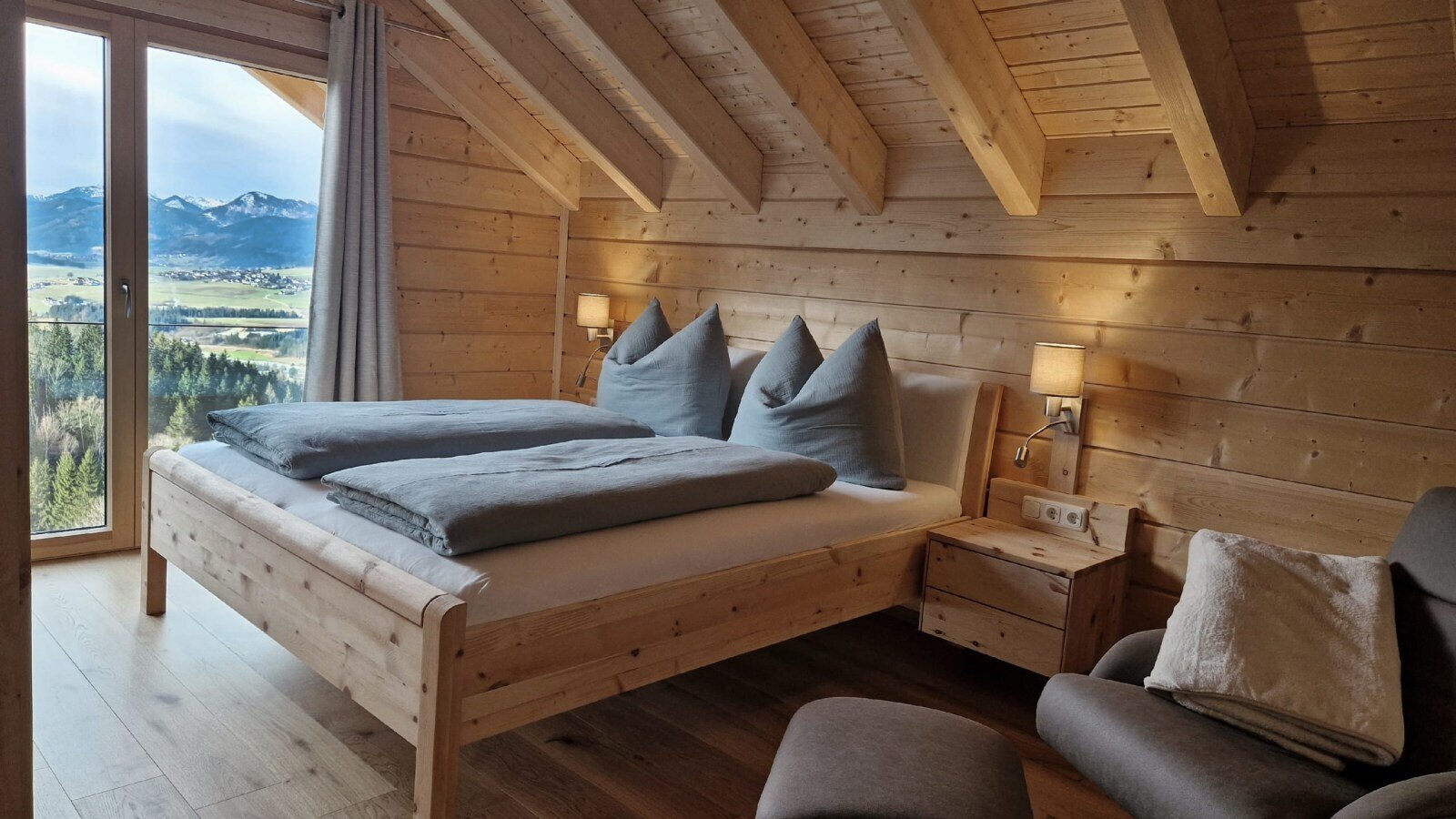 Double bedroom in the farmhouse with wooden walls, exposed ceiling beams, and a large window offering mountain views.