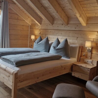 Double bedroom in the farmhouse with wooden walls, exposed ceiling beams, and a large window offering mountain views.