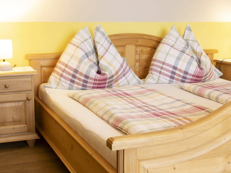A cozy double bed made of light wood in the farmhouse, featuring plaid bedding and warm bedside lamps.