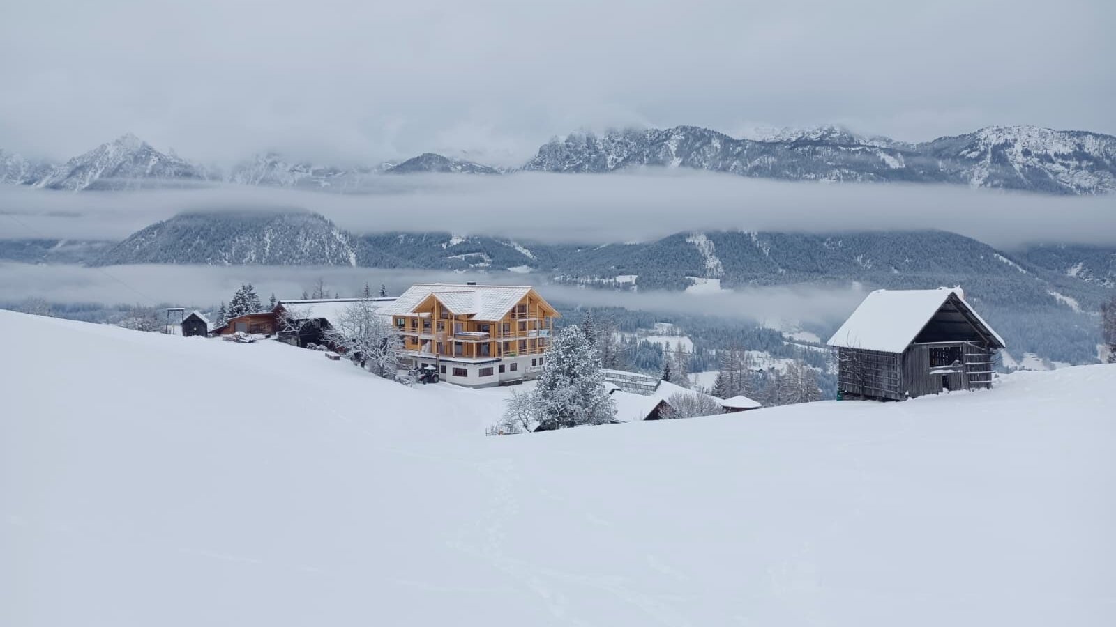 The new farmhouse in a snowy winter landscape with mountains in the background.