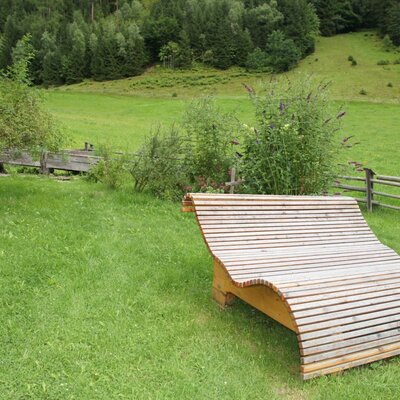 Wooden lounge chair on the farmhouse lawn with a view of the green hills and forest.