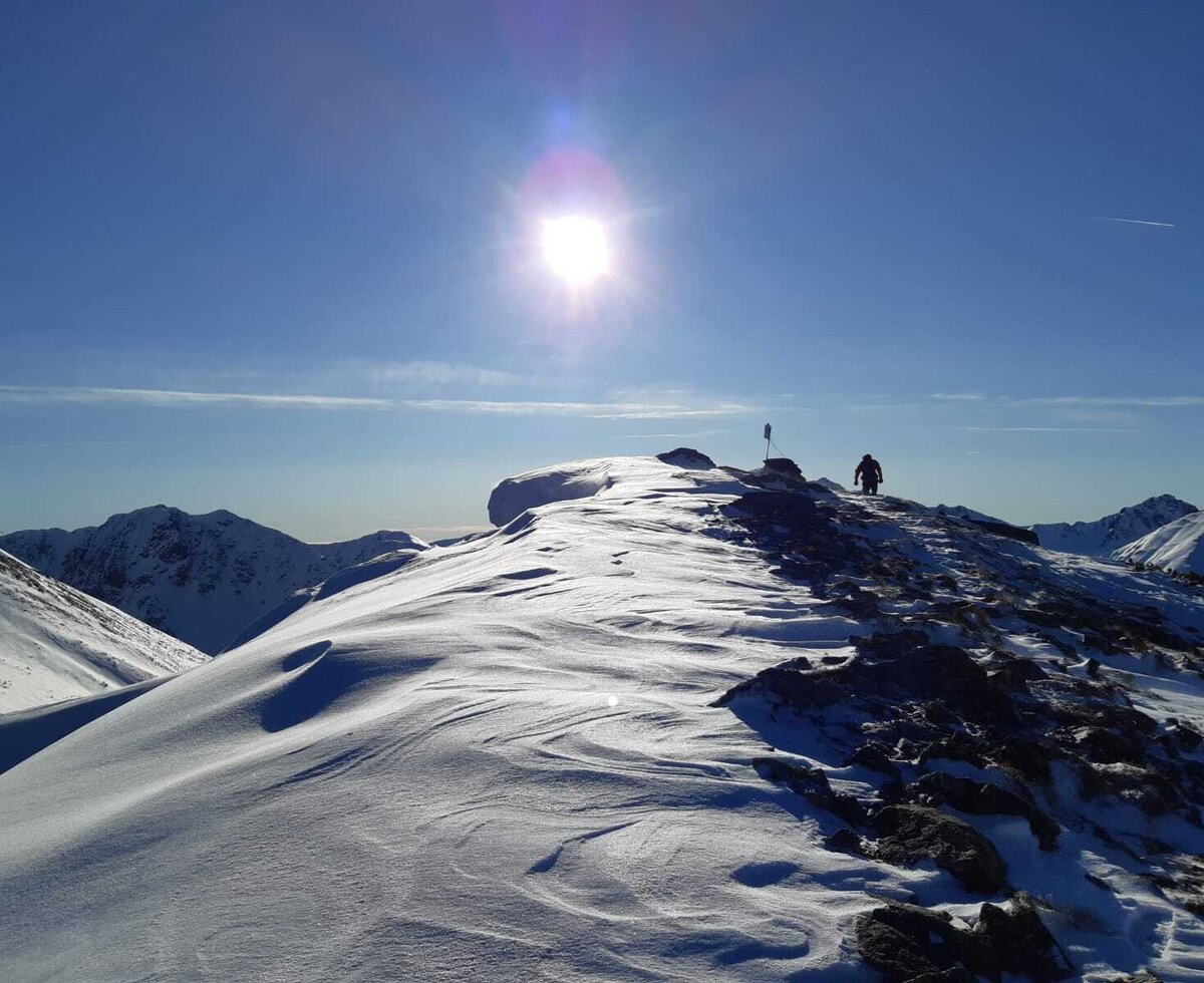 A hiker on a snowy mountain ridge under a bright sun, highlighting winter activity options accessible from the Farm House.