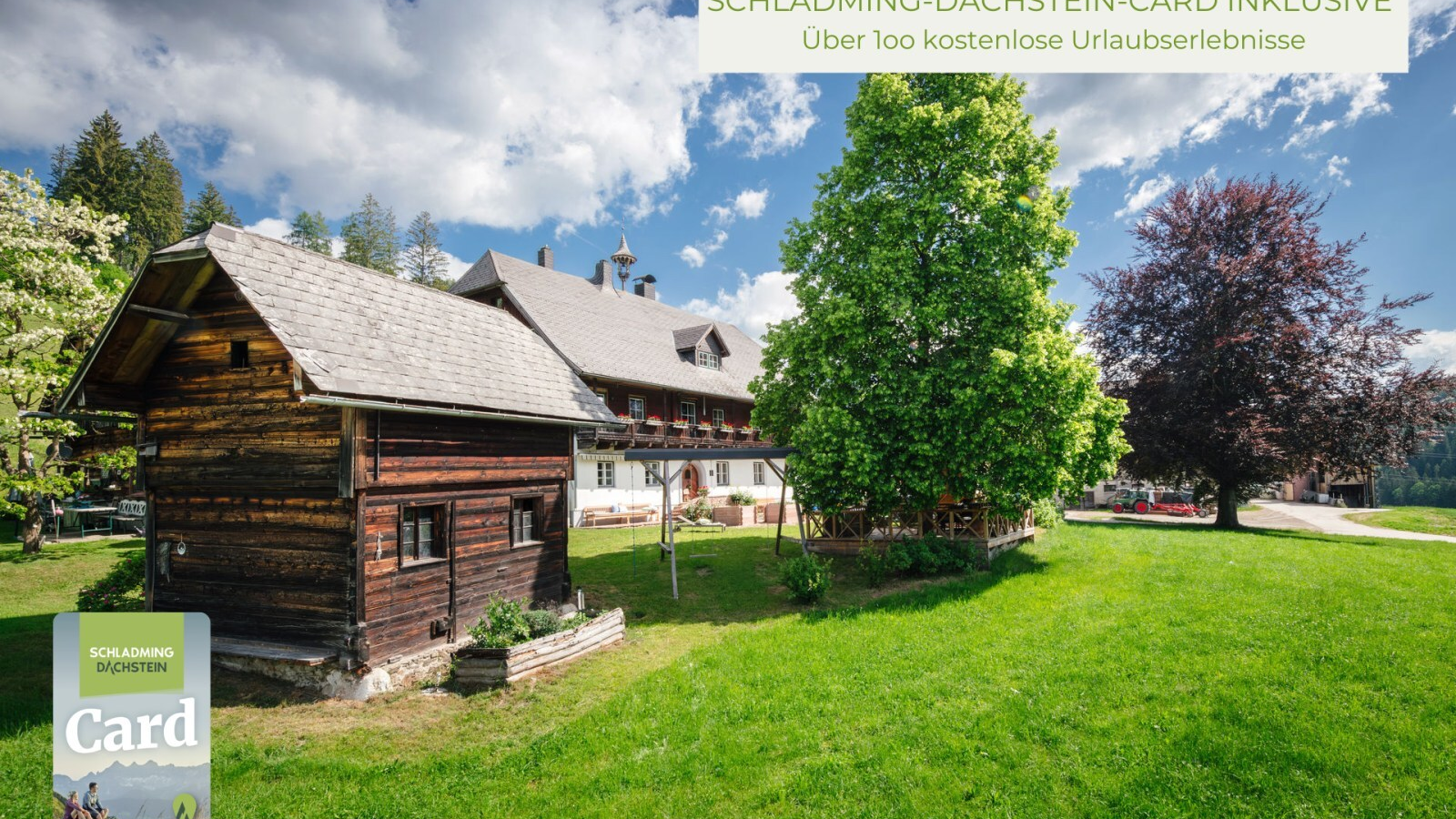 The farmhouse featuring its traditional main building with balconies and flower boxes, an outbuilding, and a large lawn.