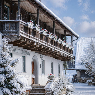 An inviting, snow-covered farmhouse featuring a traditional wooden balcony under a blue sky.