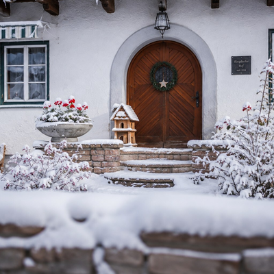 The farmhouse's inviting, snow-covered entrance, featuring a rustic wooden door and charming winter decorations.