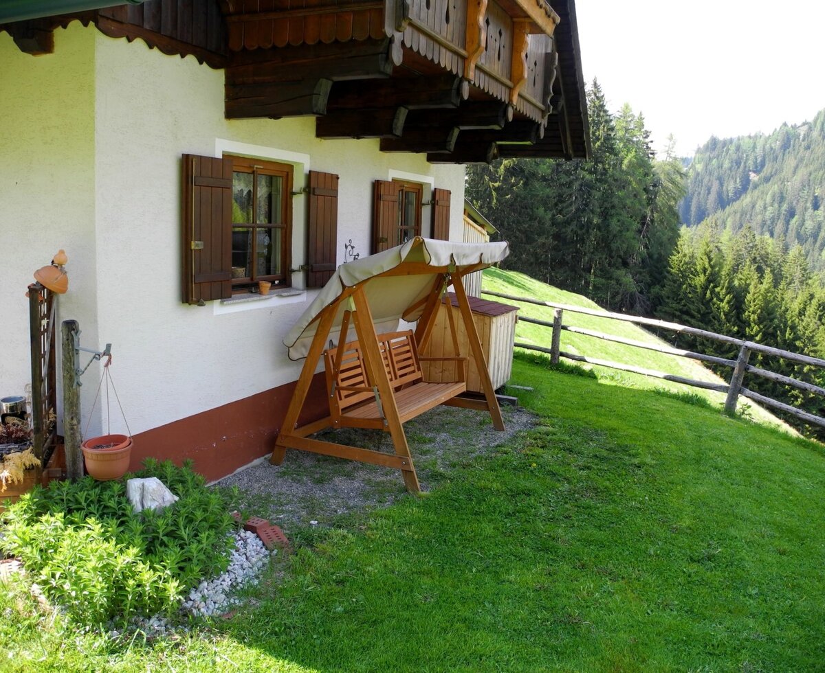 The farmhouse exterior offers a wooden swing seat, a grassy area, and a view of the forested hillside.