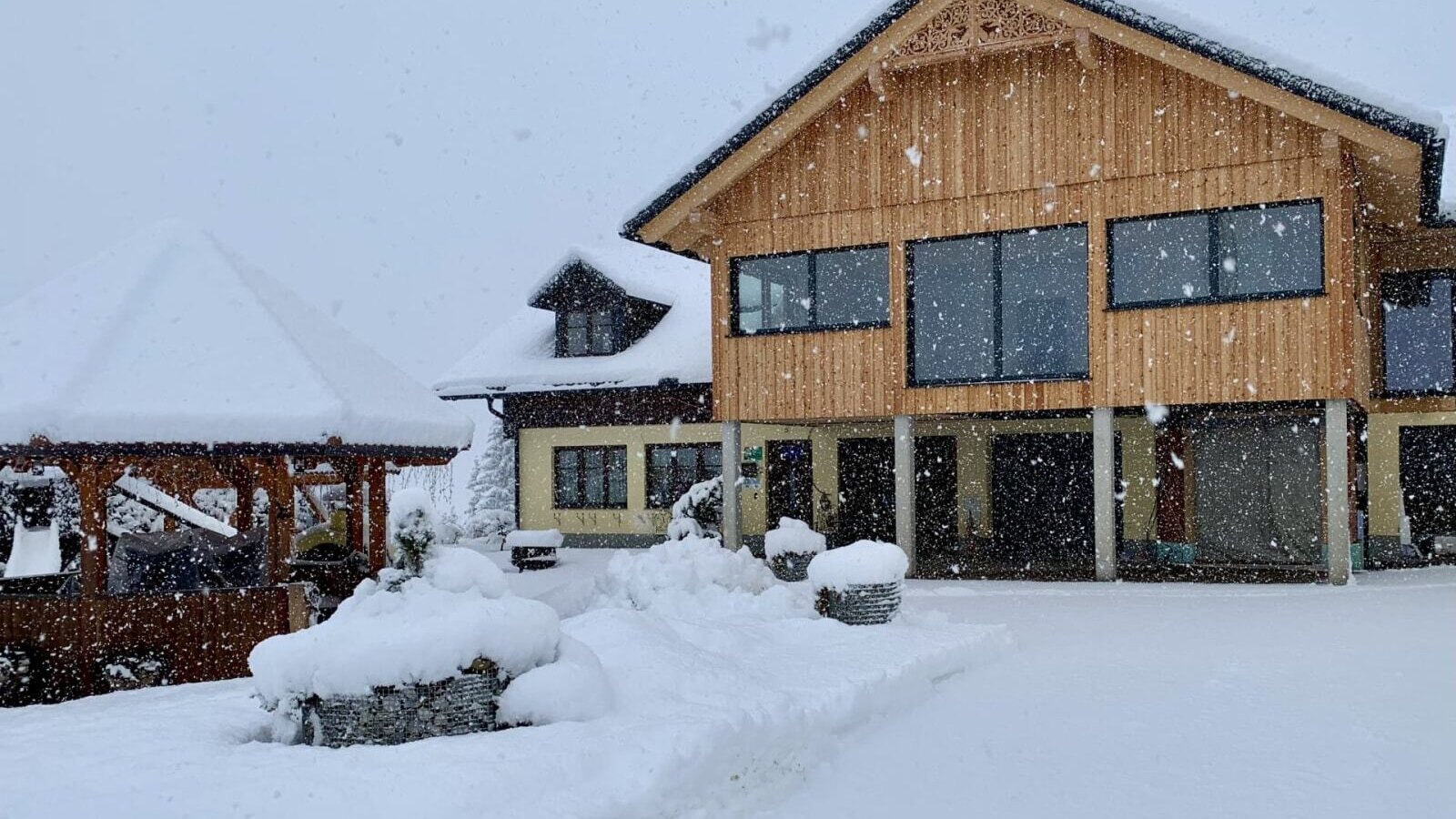 Exterior of the farmhouse in winter, featuring a snow-covered building and a wooden gazebo.