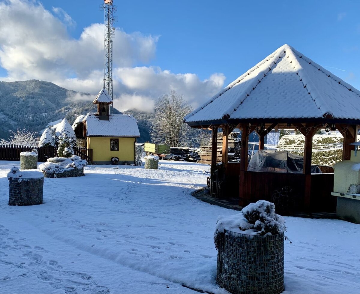 The snowy outdoor area of the farmhouse, featuring a gazebo, outdoor grill, and a small chapel.