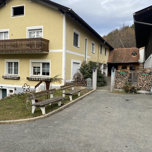 The exterior of the Farm House, featuring the main building with a balcony, outdoor benches, and an adjacent farm building.
