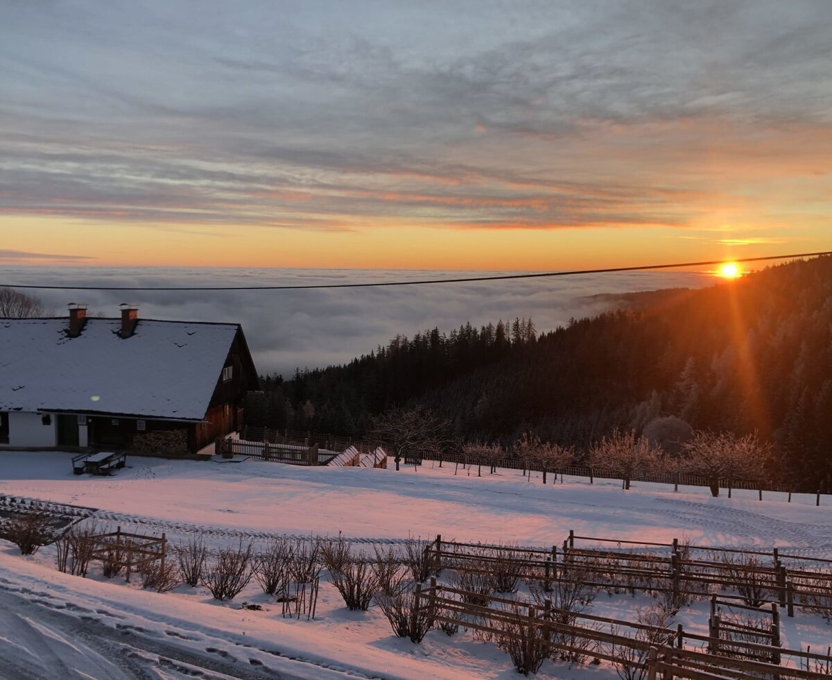 The snow-covered farmhouse at sunset above a sea of clouds.