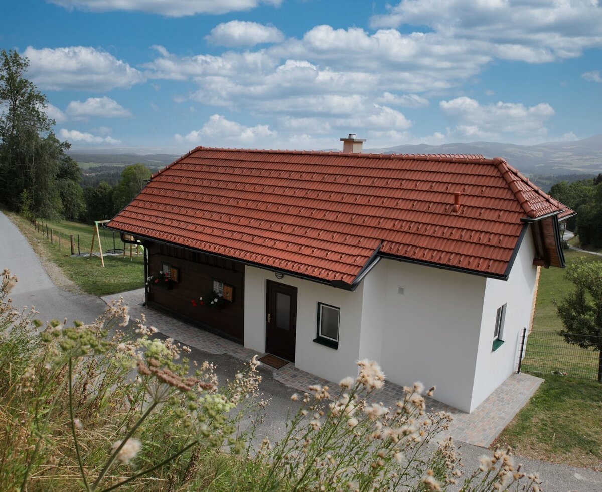 The farm house exterior features a red tiled roof, white walls, and a paved access path, with a swing set for guests and views of the countryside and distant mountains.